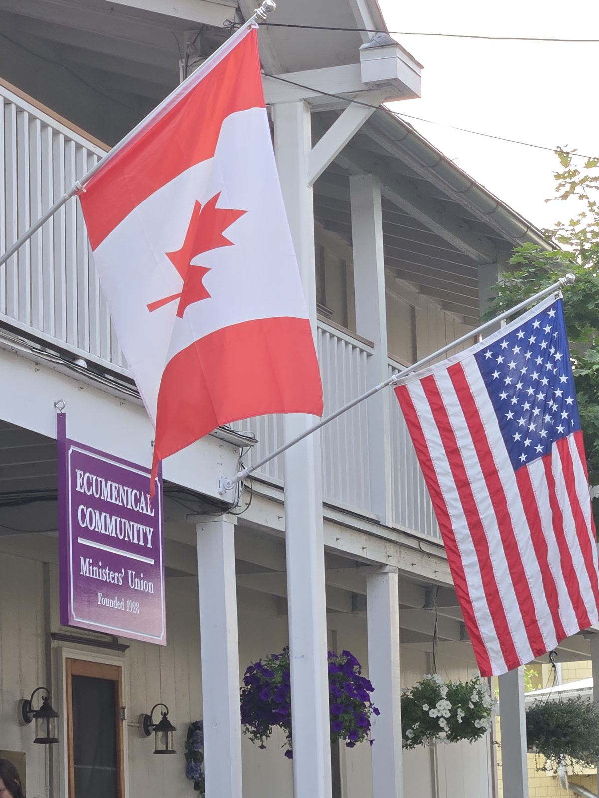 A porch flying Canadian and American flags above a sign reading Ecumenical Community